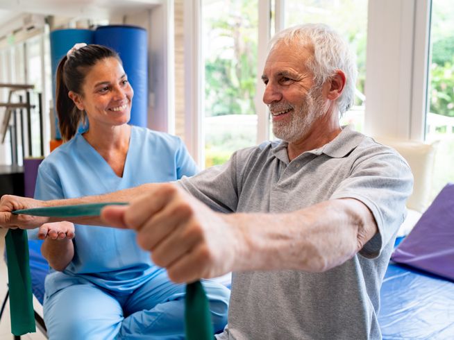 A senior man doing exercises with a resistance band alongside a physical therapist.