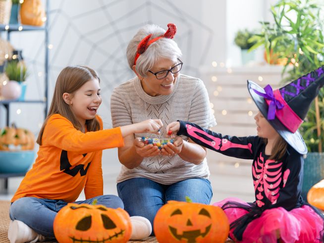 Senior woman giving candy to grandchildren on Halloween in costumes.