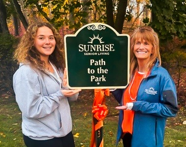 Girl scout and Sunrise Team member hold new park path sign