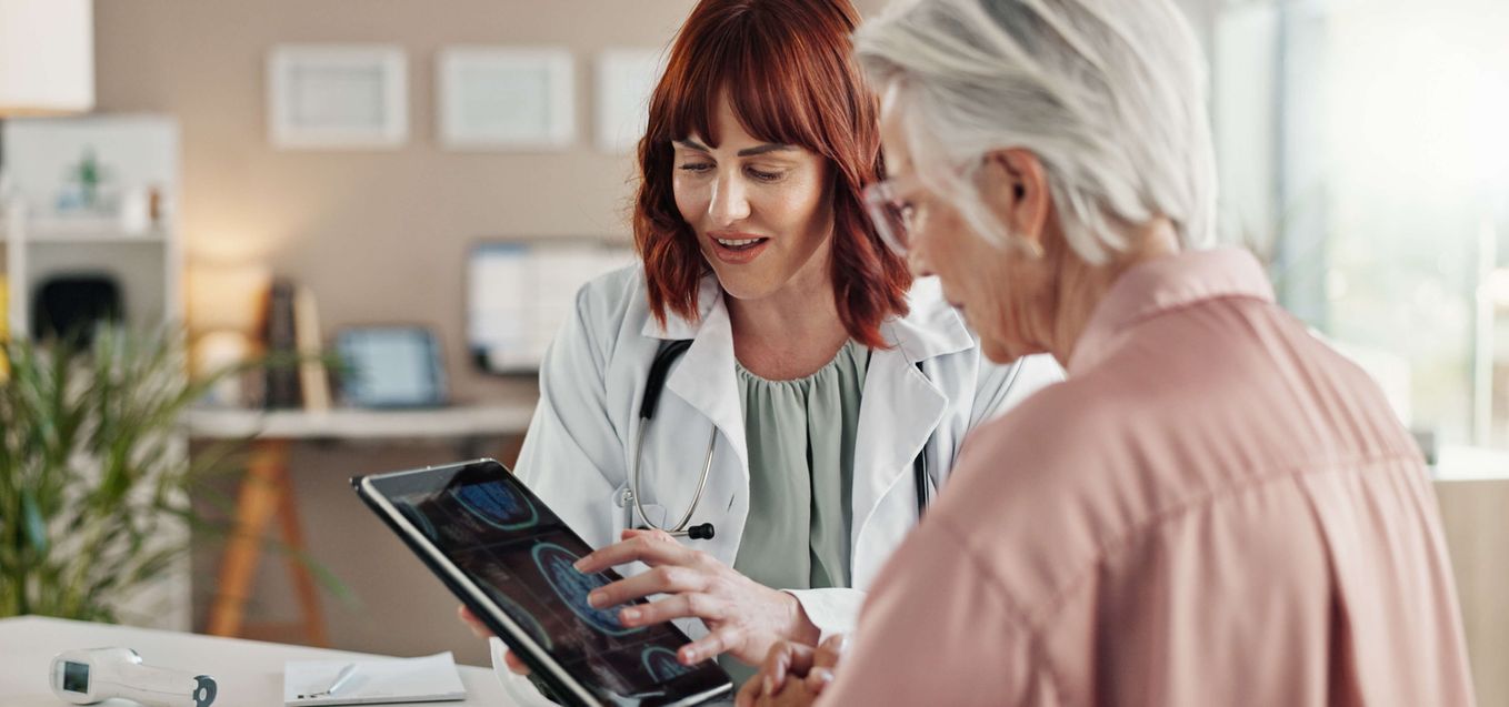 Doctor showing senior woman with dementia brain scans on a tablet