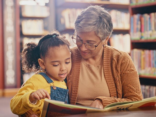 Senior woman reading a book to a child in a library.